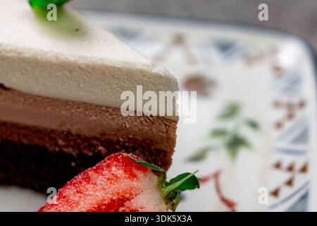 Exquisites, helles und luftiges mehrlagiges Dessert mit „drei Pralinen“ auf einem weißen Teller. Eine vertikale Nahaufnahme zeigt die zarte Textur Stockfoto