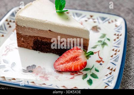 Exquisites, helles und luftiges mehrlagiges Dessert mit „drei Pralinen“ auf einem weißen Teller. Eine vertikale Nahaufnahme zeigt die zarte Textur Stockfoto