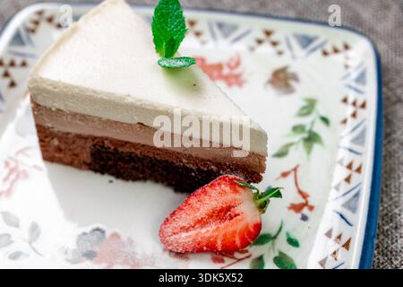 Exquisites, helles und luftiges mehrlagiges Dessert mit „drei Pralinen“ auf einem weißen Teller. Eine vertikale Nahaufnahme zeigt die zarte Textur Stockfoto