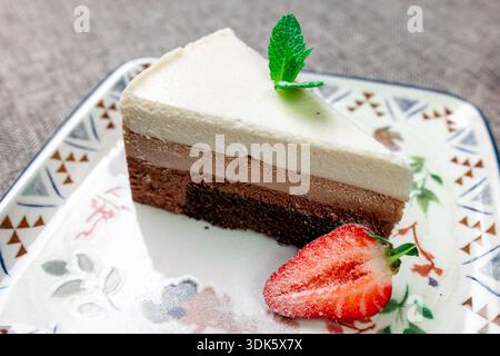 Exquisites, helles und luftiges mehrschichtiges Dessert mit „drei Pralinen“ auf einem weißen Teller. Eine vertikale Nahaufnahme zeigt die zarte Textur von Dunkelheit, Stockfoto