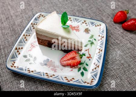 Exquisites, helles und luftiges mehrlagiges Dessert mit „drei Pralinen“ auf einem weißen Teller. Eine vertikale Nahaufnahme zeigt die zarte Textur Stockfoto