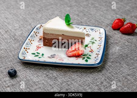 Exquisites, helles und luftiges mehrlagiges Dessert mit „drei Pralinen“ auf einem weißen Teller. Eine vertikale Nahaufnahme zeigt die zarte Textur Stockfoto