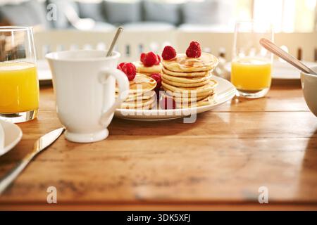 Ernährung, Pfannkuchen und Saft auf dem Tisch im Haus für hausgemachtes Frühstück, Morgenmahlzeit und Protein. Himbeeren, Essen und süße Leckereien mit Getränk in Stockfoto