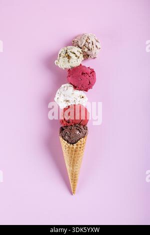 Verschiedene Eislöffel, gestapelt auf Waffelkegel vor pastellfarbenem Hintergrund Stockfoto