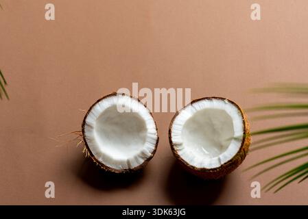 Eine frische, halbierte Kokosnuss sitzt neben drei ganzen Kokosnüssen auf braunem Hintergrund und erzeugt natürliche Schatten für Tiefe und Kontrast. Die Komposition Hi Stockfoto