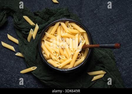 Ungekochte italienische Penne-Pasta in einer schwarzen Schüssel auf dunklem Hintergrund Stockfoto