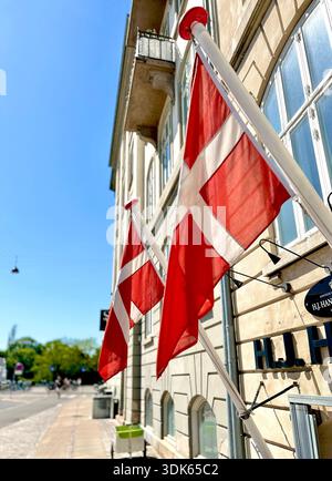 Kleine dänische Flagge an einer Gebäudefassade in Kopenhagen, die der städtischen Straßenlandschaft ein subtiles nationales Detail verleiht. Stockfoto