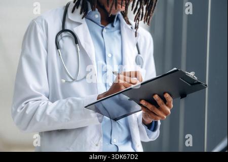 Schreiben der Informationen in den Notizblock. Nahaufnahme des Arztes im Mantel im Innenbereich. Stockfoto