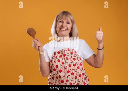Mit roter Schürze. Die ältere Hausfrau steht vor dem Hintergrund. Stockfoto