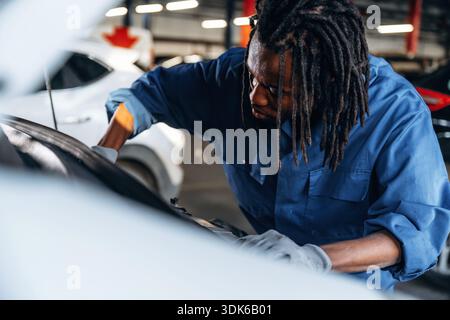 Das Auto wird unter der Motorhaube befestigt. Männlicher Mechaniker ist mit Auto in der Garage. Stockfoto