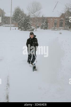Teenager, der im Winter mit einer elektrischen Schaufel Schnee von der Auffahrt entfernt. Stockfoto