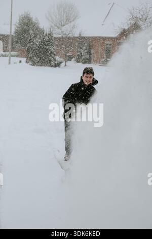 Teenager, der im Winter mit einer elektrischen Schaufel Schnee von der Auffahrt entfernt. Stockfoto