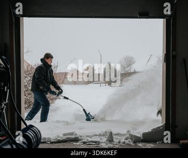 Teenager, der im Winter mit einer elektrischen Schaufel Schnee von der Auffahrt entfernt. Stockfoto