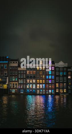 Berühmte Tanzhäuser von Amsterdam bei Nacht mit bunten Lichtern, die sich im Kanal spiegeln, Niederlande Stockfoto
