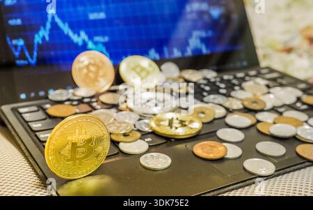 Bitcoin- und Währungsmünzen sind auf der Computertastatur verstreut und auf dem Laptop-Bildschirm sind Devisenkarten für Kryptowährungen vorhanden. Stockfoto