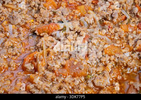 Close-up gemahlenes Rindfleisch Bolognese, sichtbare Karottenstückchen und Glanz des Olivenöls, grobe gehackte Textur, hausgemachte Kochsauce unter Rühren für Nudelnacht, c Stockfoto