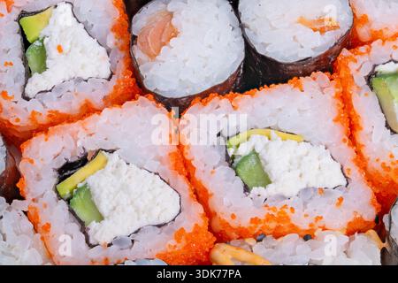 Sushi-Brötchen aus der Nähe mit Avocado und Frischkäse, tobikogesprenkelter Außenschicht und klebrigen Reiskörnern, gehobenes Geschmacksmenü mit lebhaften Farben und Stockfoto