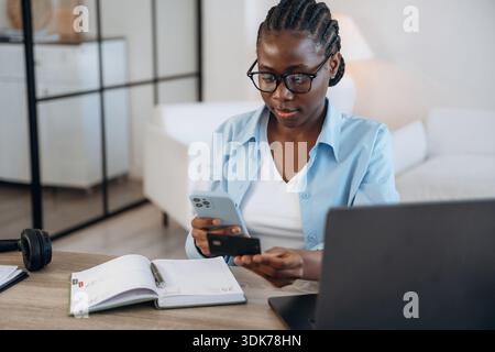 Online-Zahlung mit Kreditkarte. Die Frau ist zu Hause im Wohnzimmer. Stockfoto