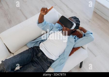 Entspannen Sie sich auf dem Sofa im VR-Headset. Die Frau ist zu Hause im Wohnzimmer. Stockfoto