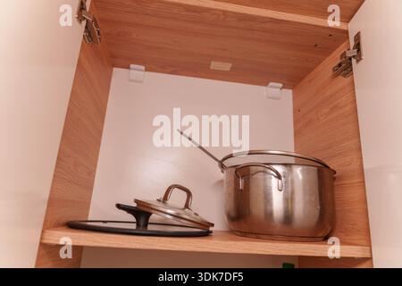 Offener Küchenschrank mit Töpfen, Tellern, Tassen und Utensilien auf Holzregalen Stockfoto