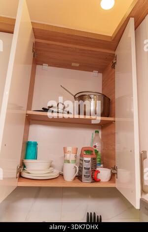 Offener Küchenschrank mit Töpfen, Tellern, Tassen und Utensilien auf Holzregalen Stockfoto