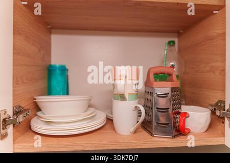 Offener Küchenschrank mit Töpfen, Tellern, Tassen und Utensilien auf Holzregalen Stockfoto