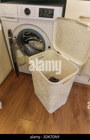 Wäschekorb mit Kleidung vor offener Waschmaschine auf Holzboden Stockfoto