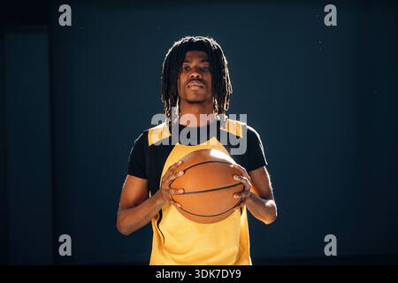 Entspannt, stehend und posiert. Der junge Schwarze spielt drinnen Basketball. Stockfoto