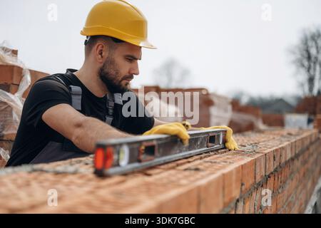 Die richtige Ebene mit dem Werkzeug einrichten. Bauarbeiter arbeiten im Freien mit Ziegeln. Stockfoto