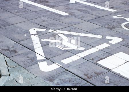 Weiße Fahrradschablone auf gefliestem Bürgersteig, Pfeil- und Dreiecksmarkierungen, die auf einen speziellen Radweg hinweisen, Nahansicht Stockfoto