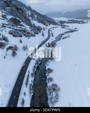 Aus der Vogelperspektive auf eine kurvenreiche Straße, die durch den schroffen weißen Schnee entlang eines Flusses führt, mit baumgesäumten Bergen, Sils im Engadin/Segl, Bündner, Switzer Stockfoto