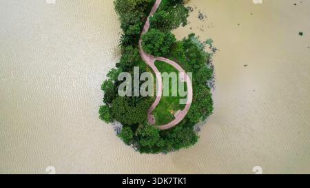 Aus dem karamellfarbenen Wasser erhebt sich eine grüne Inseloase, gespickt mit gewundenen Wegen, eine ruhige Zuflucht im Herzen der Stadt, Abuja, Fe Stockfoto