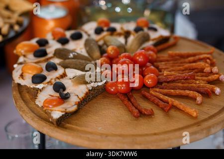 Verschiedene Vorspeiseteller mit Toast aus geräuchertem Lachs, Gurken, Oliven, Kirschtomaten und Würstchen auf einer hölzernen Servierplatte Stockfoto