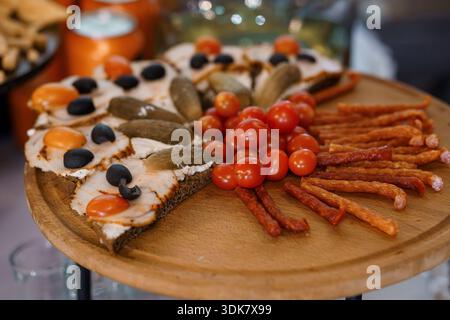 Verschiedene Vorspeiseteller mit Toast aus geräuchertem Lachs, Gurken, Oliven, Kirschtomaten und Würstchen auf einer hölzernen Servierplatte Stockfoto