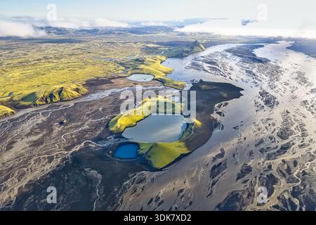 Aus der Vogelperspektive auf Gletscherflüsse, die sich durch die Landschaft schlängeln, im Kontrast zu lebendigem grünem Moos und ruhigen blauen Seen, Skaftárhreppur, Island. Stockfoto