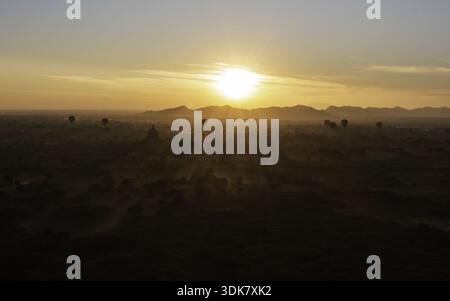 Aus der Vogelperspektive sehen Sie Heißluftballons, die sanft über die antiken Tempel und Pagoden schweben, umgeben von dem goldenen Licht der aufgehenden Sonne, Old Bagan, Manda Stockfoto