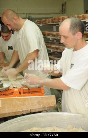 Bäckereiarbeiter, die Brotteig auf Holztischen in einer traditionellen Bäckerei in Baligród, Polen, Formen und wiegen. Stockfoto