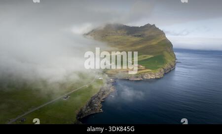 Aus der Vogelperspektive treffen Sie auf das tiefblaue Meer, umgeben von ätherischen Nebeln in der Nähe der grünen Länder, Torshamn, Färöer Inseln. Stockfoto