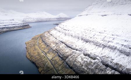 Aus der Vogelperspektive schneebedeckte Gipfel und Klippen treffen auf das blaue Wasser und schaffen einen ruhigen Kontrast in der Landschaft, Torshavn, Färöer Inseln. Stockfoto