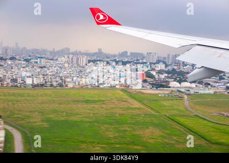 Blick aus einem Flugzeugfenster, auf einen Flügel, Flugzeuglande, Flug über eine Stadt mit Wohnhäusern und grünen Feldern. Vietnam, Ho-Chi-Minh-Stadt Stockfoto