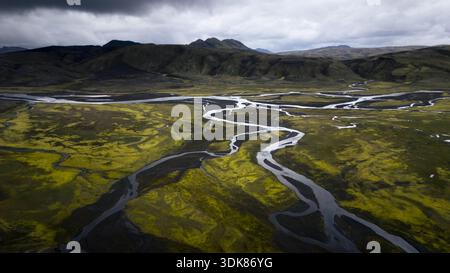 Aus der Vogelperspektive auf Gletscherflüsse, die sich durch die lebendige grüne und schwarze Landschaft unter einem glühenden Himmel schlängeln, Selfoss, Island. Stockfoto