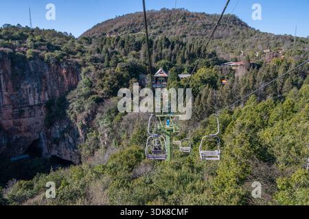 Der Blick auf die Landschaft vom Sessellift in der Yiliang Jiuxiang Höhle und den Eingang in die Höhle am Fuße der Karstklippe. Stockfoto