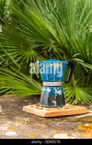 Verwitterter Camping-Mokakopf auf Stein im Freien mit Palmen Hintergrund, repräsentiert Reisen, Abenteuer, Outdoor-Kaffee, minimalistischen Lebensstil und langsam Stockfoto