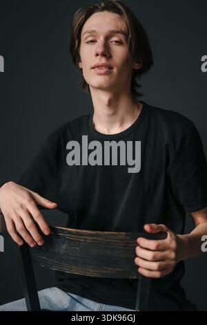 Selfassured Mann, der direkt mit strukturiertem Holzstuhl-Hintergrund blickt Stockfoto