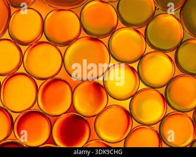 Lebendige Nahaufnahme überlappender Öltröpfchen in Orange- und Gelbtönen. Die lichtdurchlässigen Blasen bilden ein warmes, abstraktes Muster, ideal für Hintergründe, DE Stockfoto