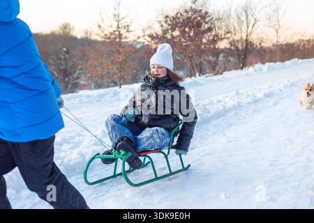 Kinder fahren gemeinsam mit Hund im verschneiten Winterpark. Freunde, Geschwister oder Familie genießen aktiven Outdoor-Winterspaß, Kinderfreude, Spiel und Bindung Stockfoto