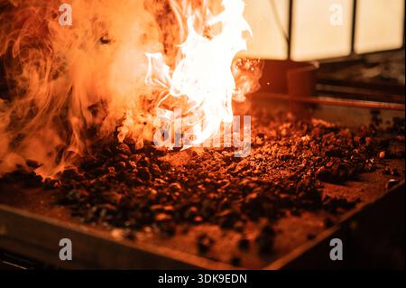 Offenes Feuer und glühende Glut in einer Schmiedeschmiede, die während eines Metallbearbeitungsprozesses in einer Industriewerkstatt intensive Hitze zeigt Stockfoto