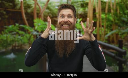 Mann ballt Fäuste und lächelt auf einer Holzbrücke in einem üppig grünen Park unter hellem Sonnenlicht; Spannung. Stockfoto