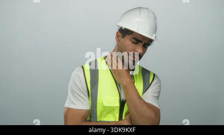Hispanischer Mann mit Helm und Neon-Sicherheitsweste Husten in der Faust im grauen Studio; Unwohlsein. Stockfoto