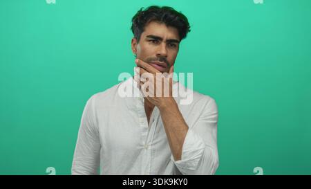Der Mann drückt die Fingerspitzen, um in nachdenklicher Pose in grünem Studio mit sanfter Richtungsbeleuchtung zu kneifen; Verwirrung. Stockfoto